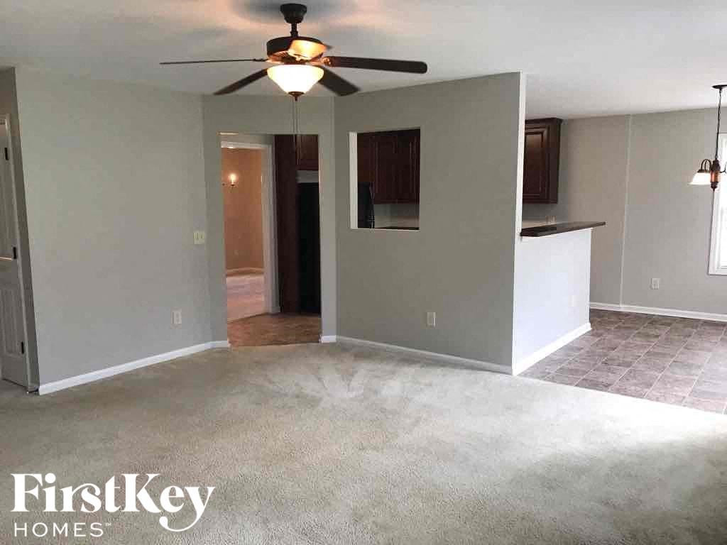an empty living room with a ceiling fan and a kitchen