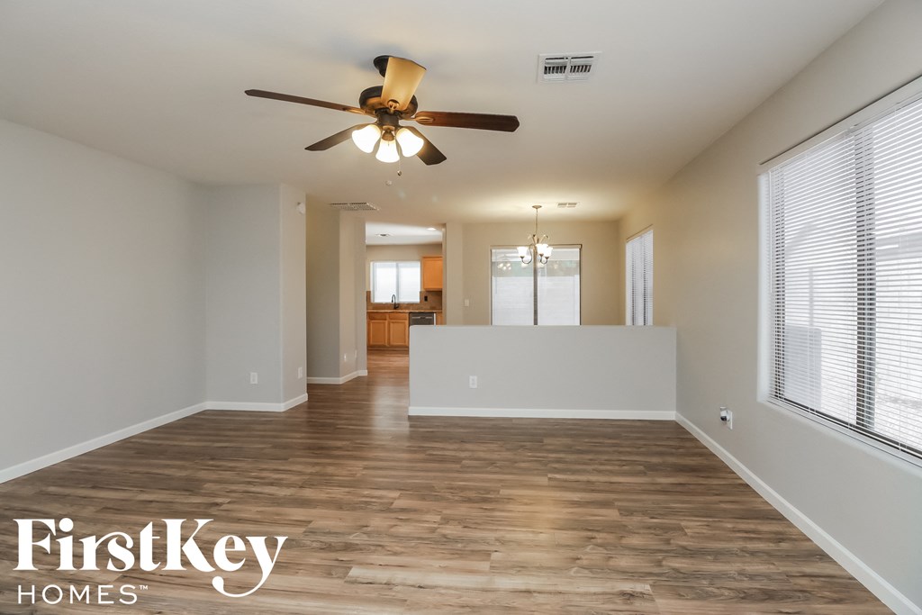 an empty living room with a ceiling fan and a kitchen