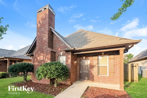 A brick house with a chimney and a tree in front.