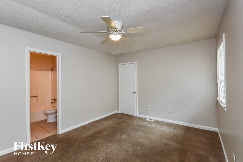 a empty living room with a ceiling fan and a door to a bathroom