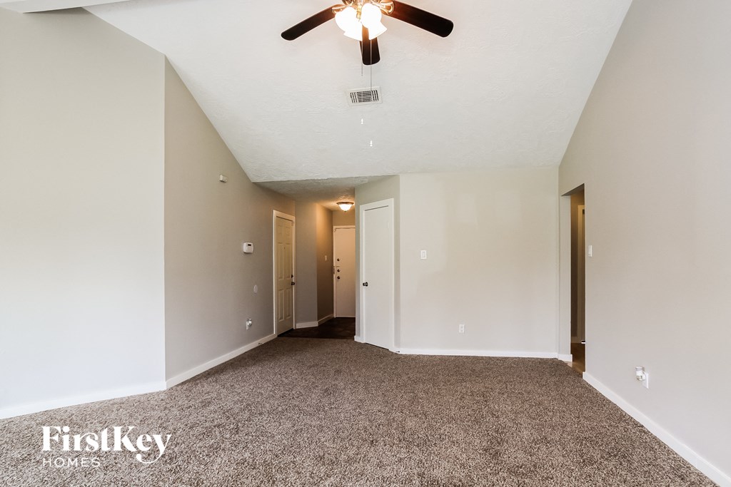 a spacious living room with carpet and a ceiling fan