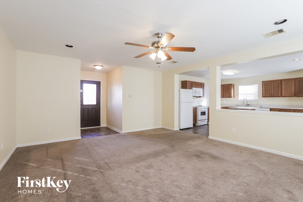 an empty living room with a ceiling fan and a kitchen
