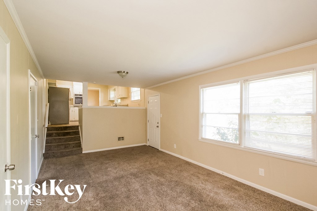 an empty living room with a kitchen in the background