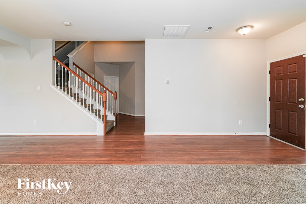 A room with a wooden floor and a staircase with a red railing.