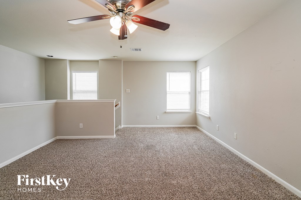 A spacious room with a ceiling fan and two windows.