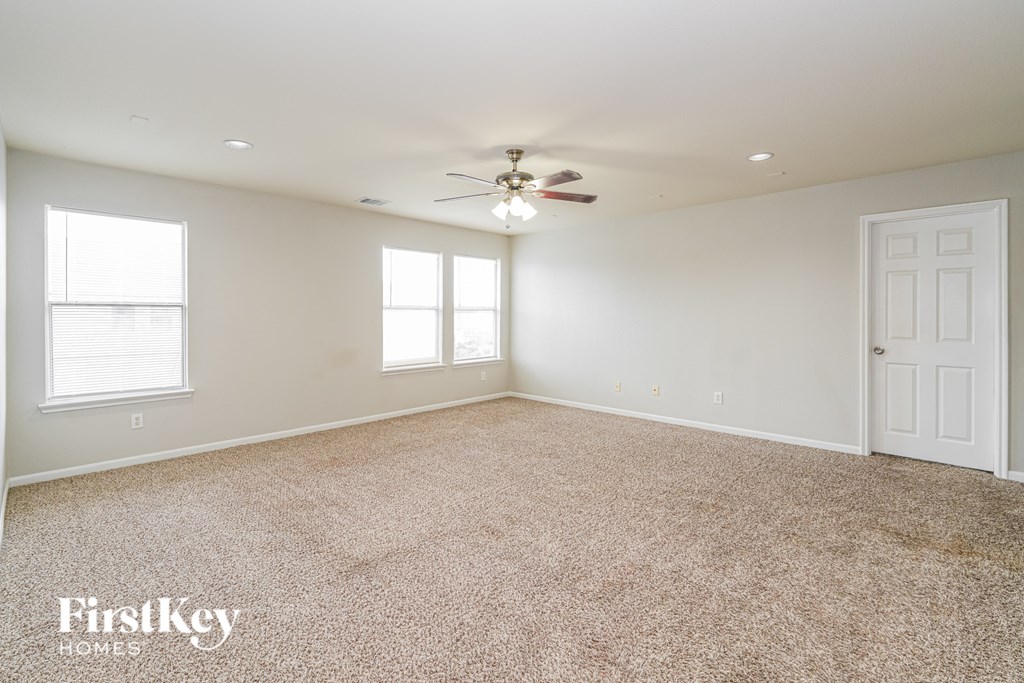 A spacious room with a carpeted floor, a ceiling fan, and a door on the right side.