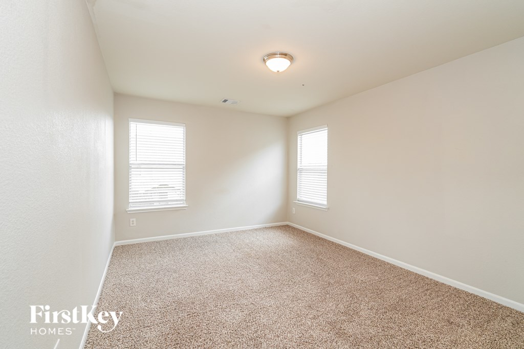 A room with a carpeted floor and two windows with blinds.
