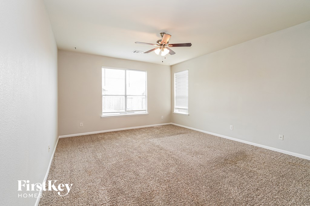 A room with a carpet floor, a ceiling fan, and a window.