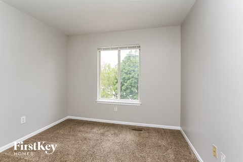 A room with a carpeted floor and a window showing trees outside.
