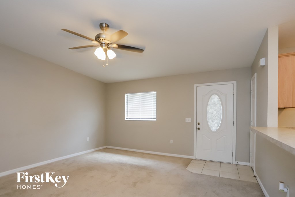 an empty living room with a ceiling fan and a white door
