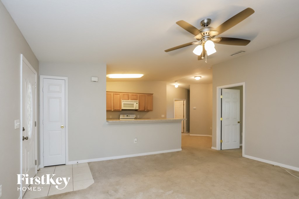an empty living room with a ceiling fan and a kitchen