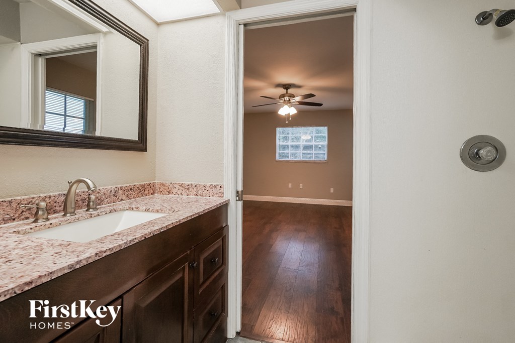 a bathroom with a sink and a ceiling fan and a door to a hallway