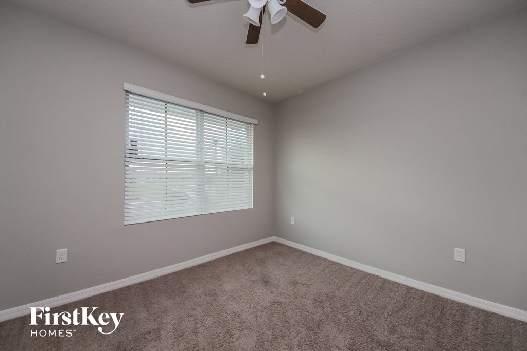 a carpeted room with a window and a ceiling fan