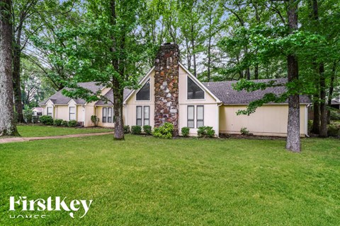 A house with a stone chimney is surrounded by trees and grass.