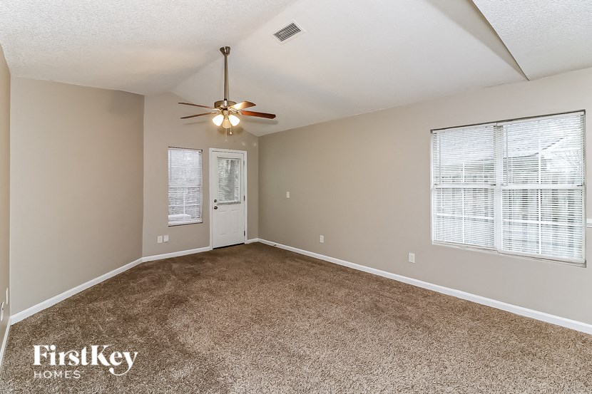 A room with a carpeted floor, a ceiling fan, and two windows with blinds.