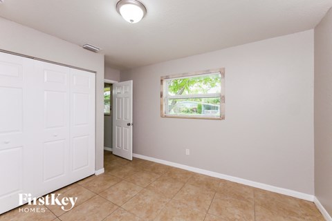 A room with a white door and a window with a view of trees.