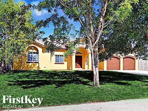 a yellow house with two garage doors and a tree in the yard