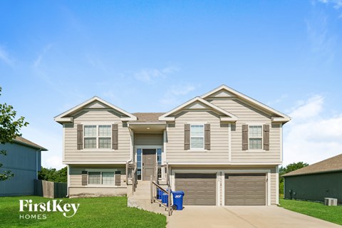 A two-story house with a garage and a blue trash bin in front.
