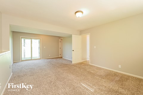 A spacious room with a carpeted floor and a window with blinds.