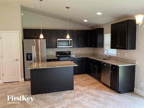 A kitchen with black cabinets and a stainless steel refrigerator.