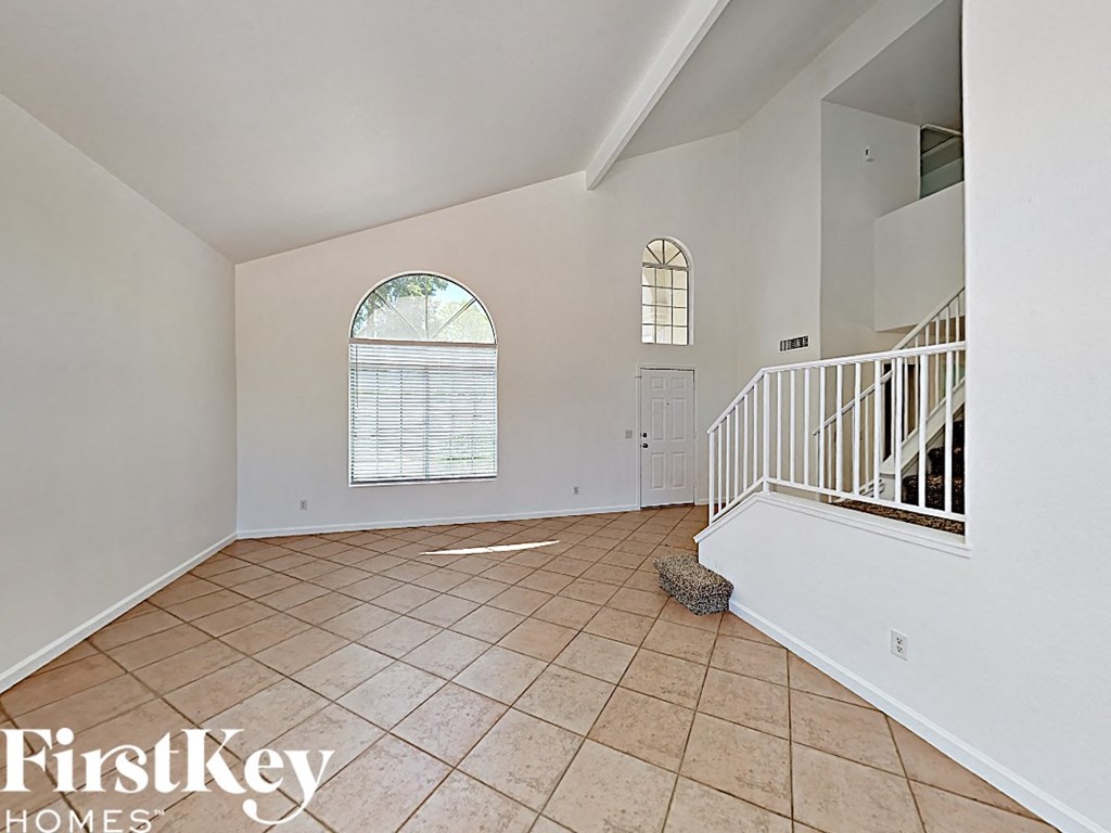 an empty living room with tile flooring and a white staircase