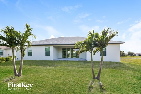 A white house with a grey roof and two palm trees in front.