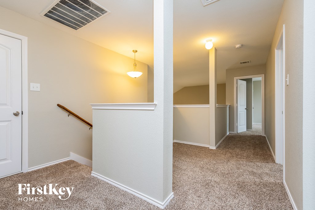 a hallway with white walls and a carpeted floor and a staircase