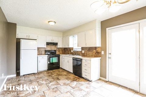 A kitchen with a white fridge, black oven, and a tiled floor.