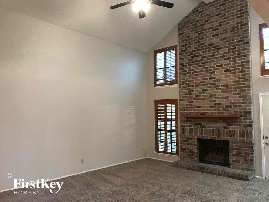 an empty living room with a brick fireplace and a ceiling fan