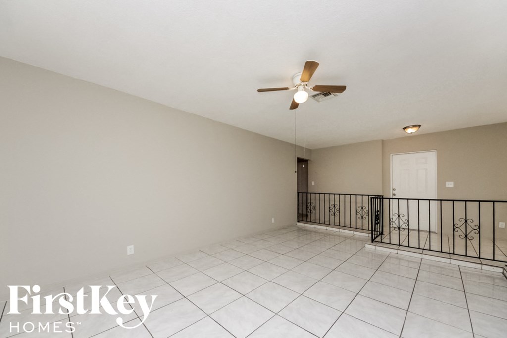 an empty living room with a ceiling fan and a balcony
