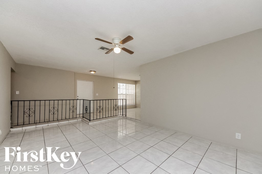 an empty living room with a ceiling fan and a balcony