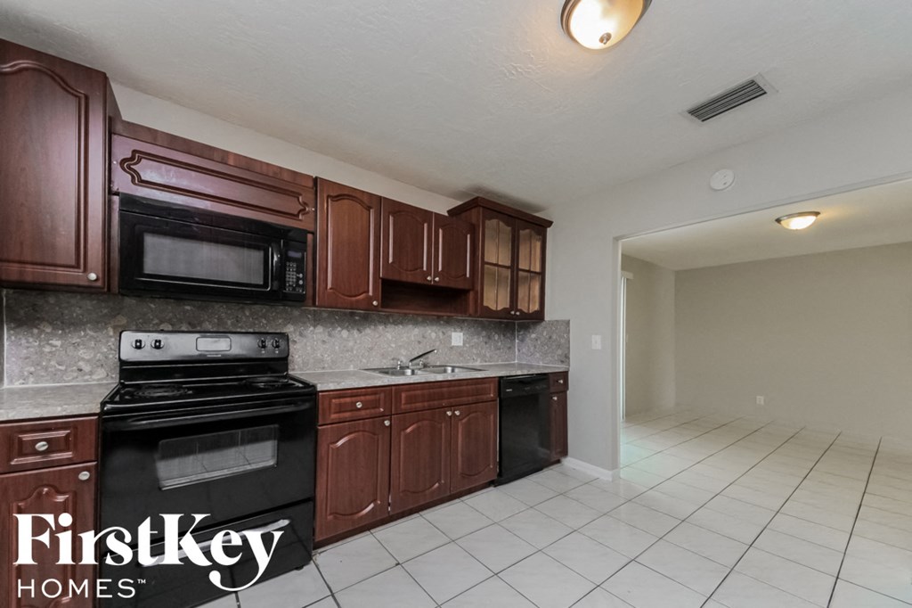 a kitchen with wood cabinets and black appliances and white tiled floors
