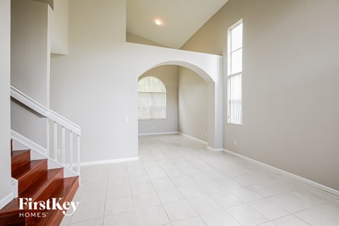 A spacious room with a staircase on the left and a window on the right.