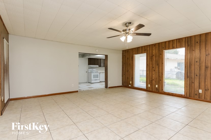 A spacious room with a ceiling fan and a kitchen area in the background.