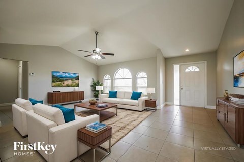 A spacious living room with a white sofa set and a ceiling fan.