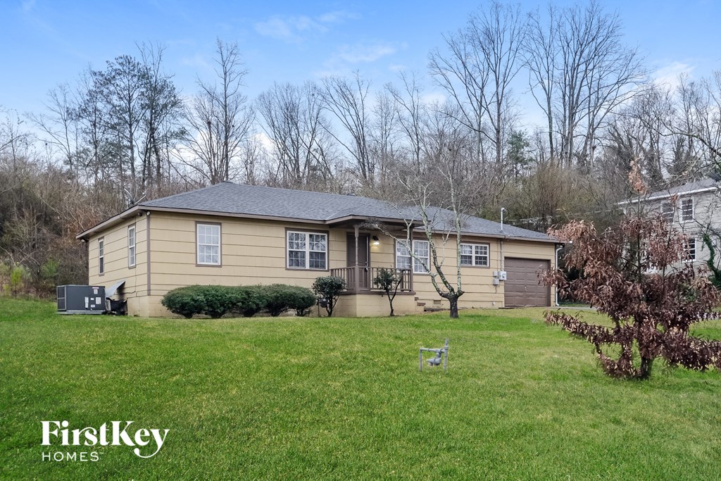 the front of a yellow house with a lawn and trees