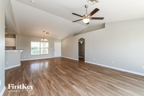 the spacious living room with hardwood flooring and a ceiling fan