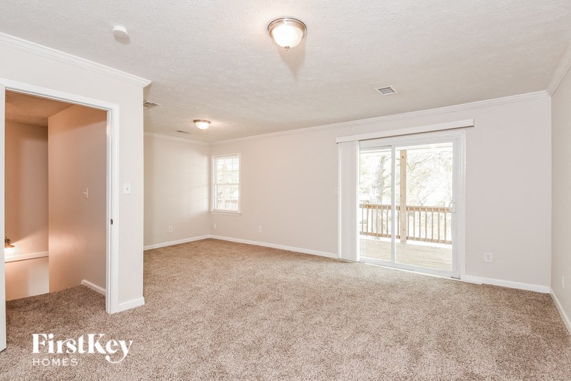 A spacious room with a carpeted floor and a sliding glass door leading to a balcony.