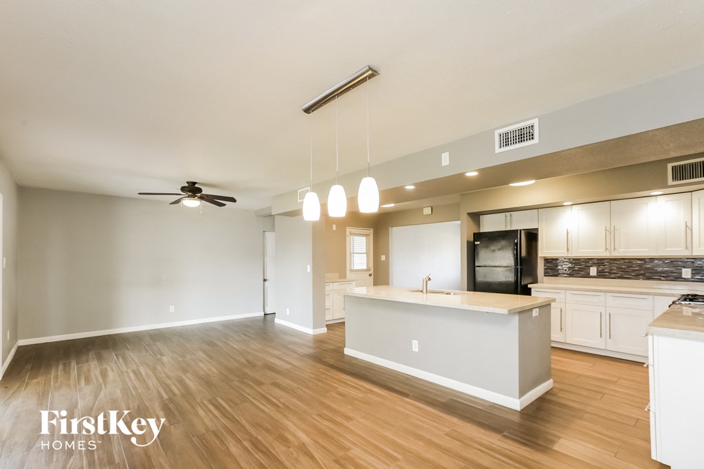 an open kitchen and living room with wood flooring and white cabinets