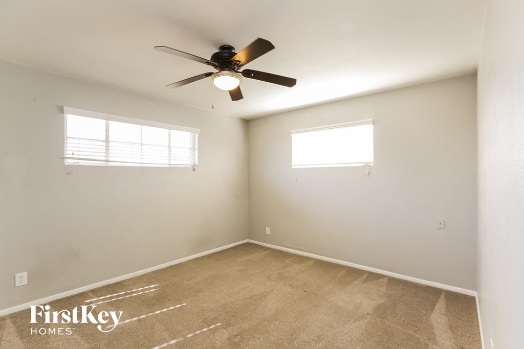 an empty room with a ceiling fan and two windows