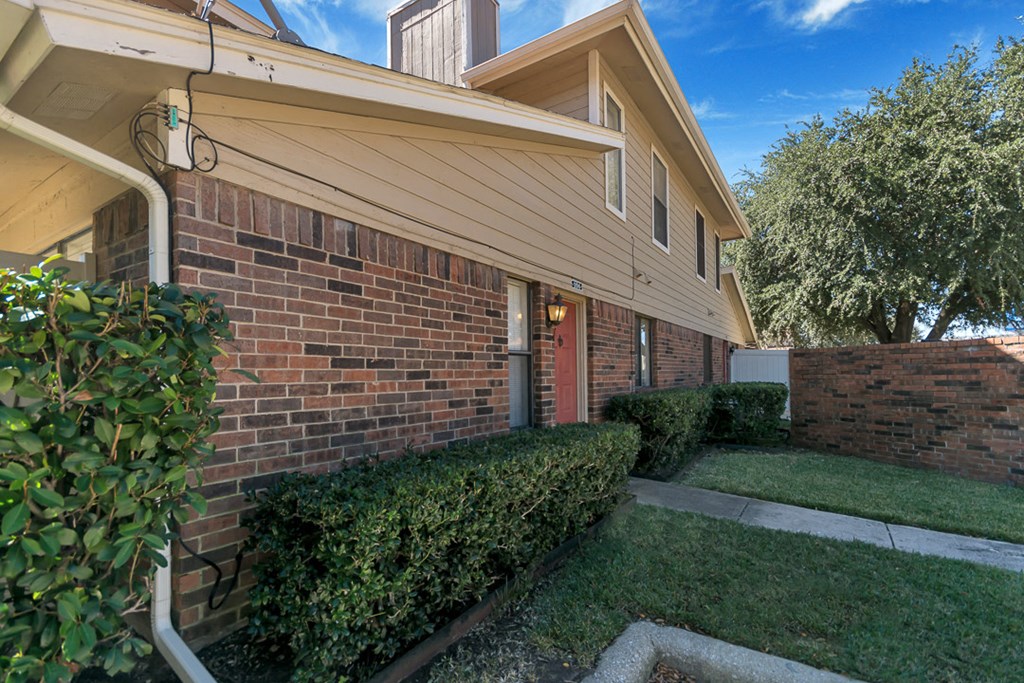 a side view of a brick house with a yard and sidewalk