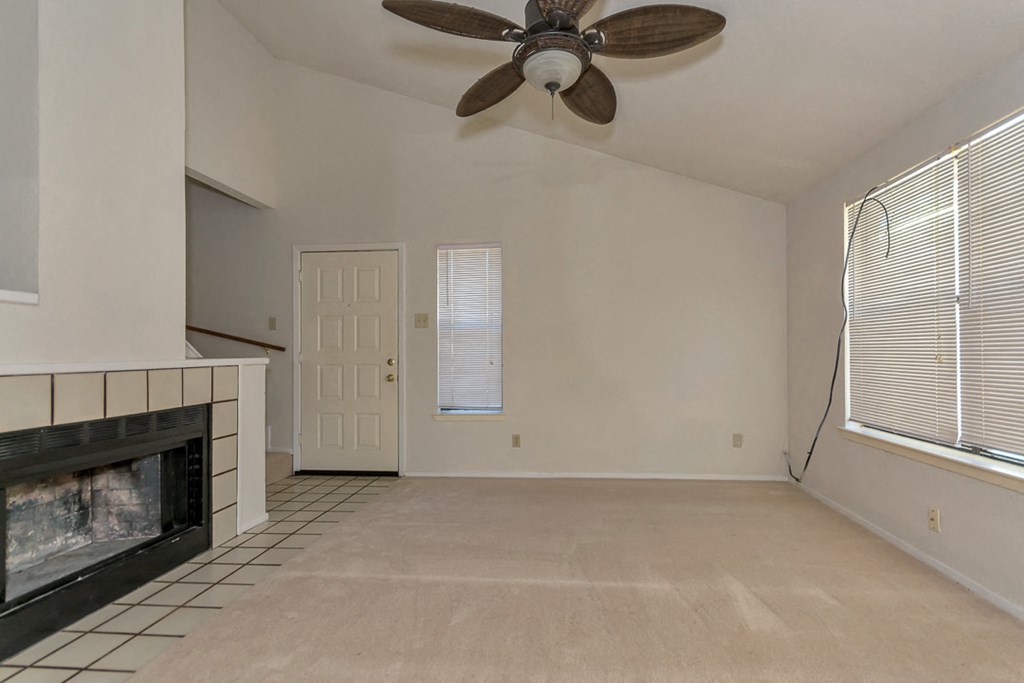 an empty living room with a fireplace and a ceiling fan