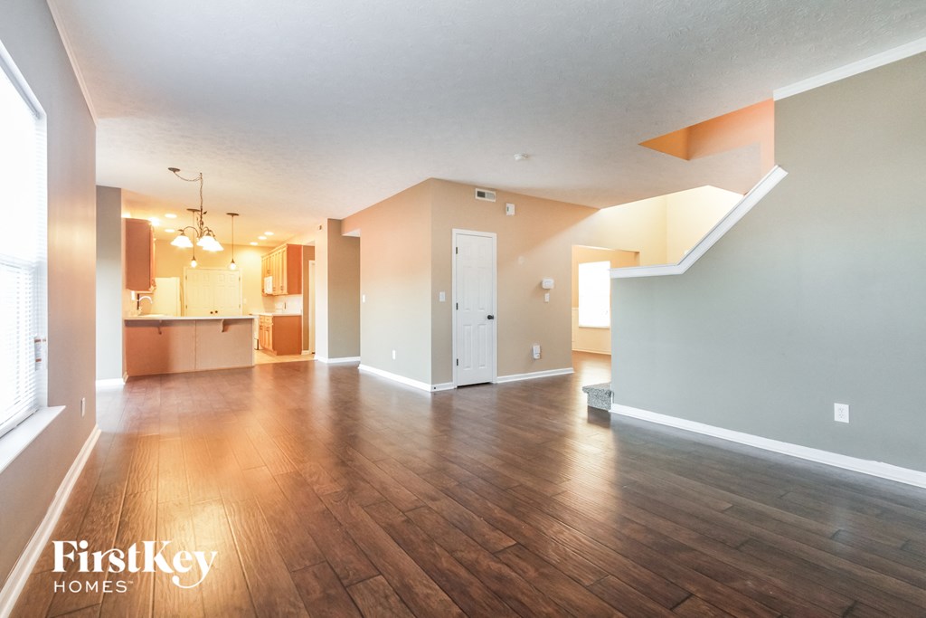 A spacious room with wooden floors and a large window on the left side.