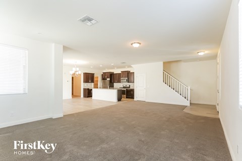 A spacious living room with a staircase on the right and a kitchen area in the background.
