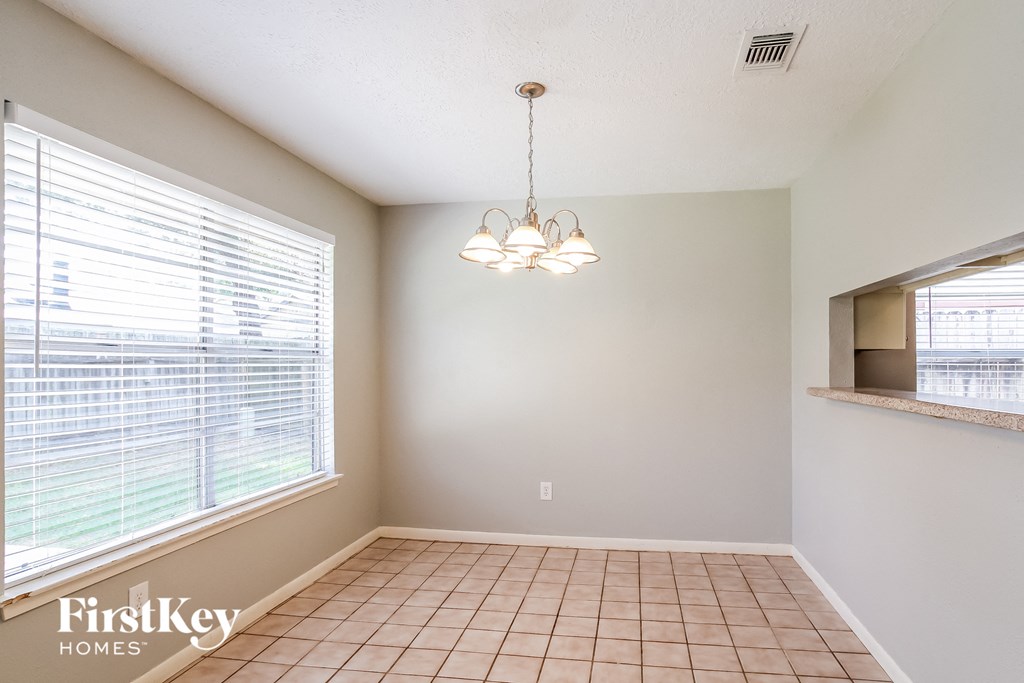 an empty dining room with a large window and a chandelier