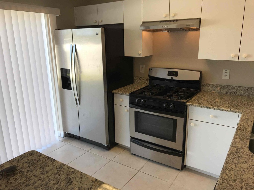 A kitchen with a stainless steel refrigerator, black stove, and white cabinets.