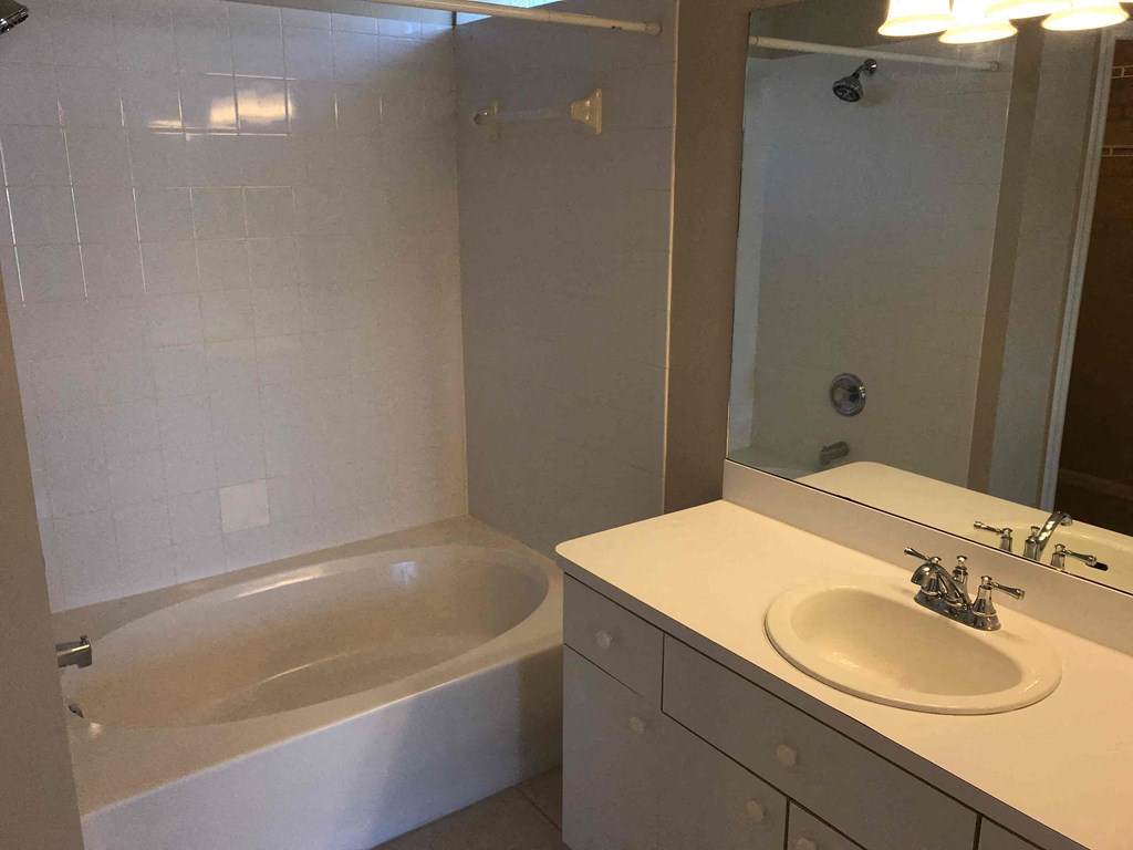 A white bathroom with a tub, sink, and mirror.