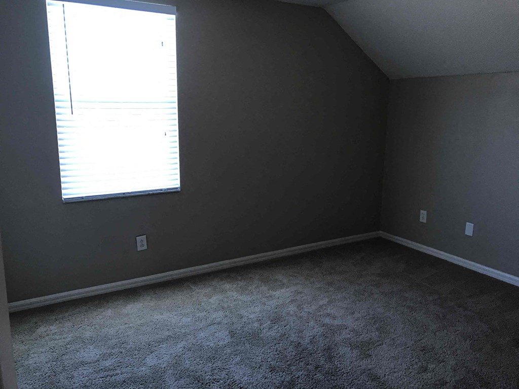 A room with a carpeted floor and a window with blinds.