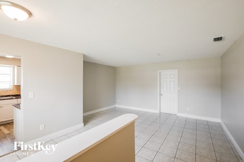 A spacious empty room with a kitchen area in the background.