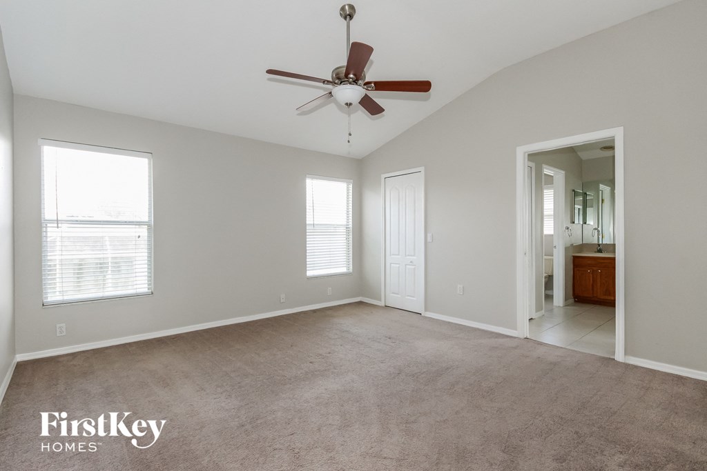 A spacious room with a ceiling fan and a view of a balcony through the window.